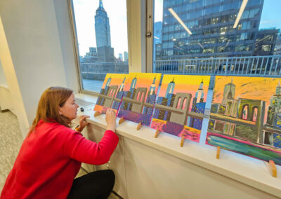 Girl doing last touches to her painting during a corporate sip and paint event in Manhattan office. Empire state building in the background.
